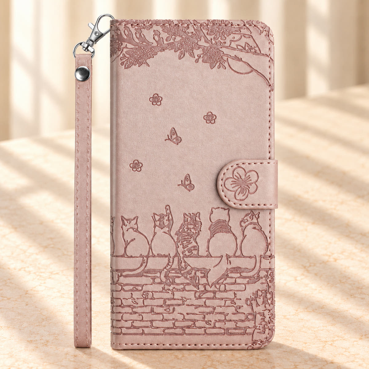 Front of the Champagne Pink Cat Garden wallet case with embossed cats, leafy branches, flower tab and wrist strap.