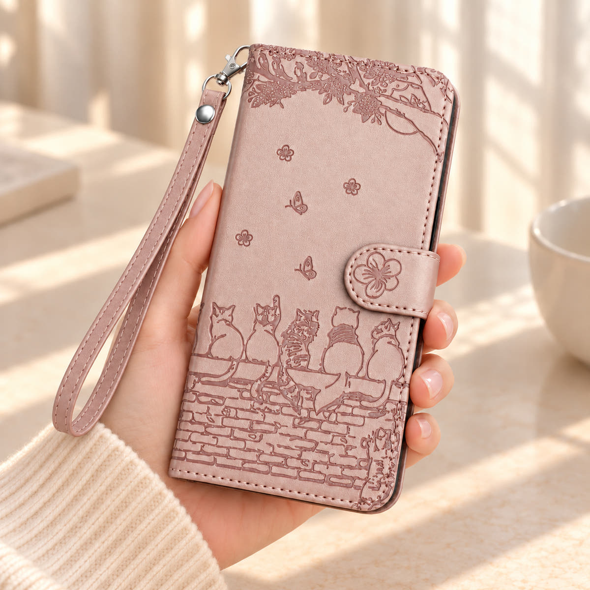 Champagne Pink Cat Garden wallet case held in one hand, showing the embossed garden scene and matching wrist strap.