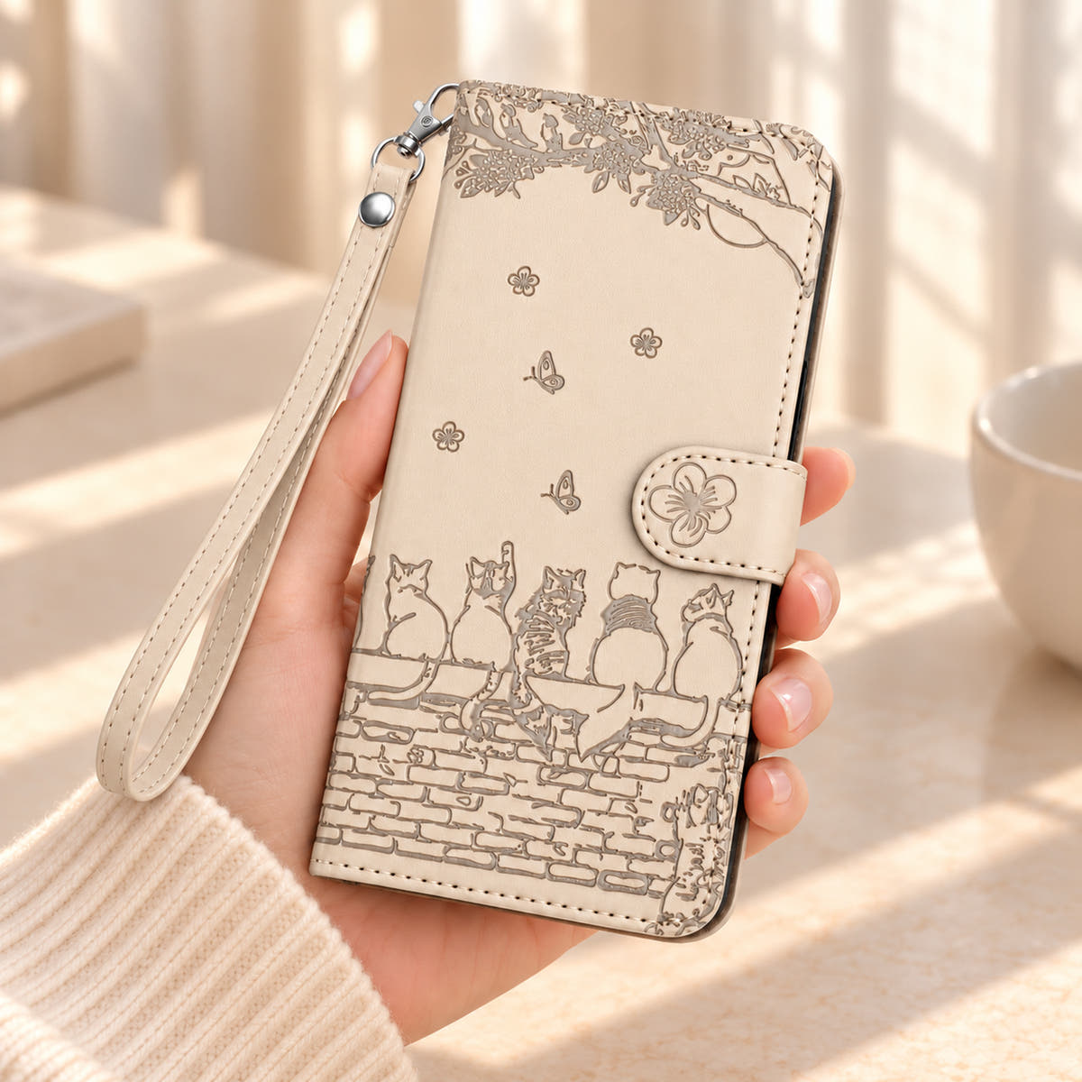 Ivory Cat Garden wallet case held in one hand, with the flower closure, embossed cats and matching wrist strap visible.