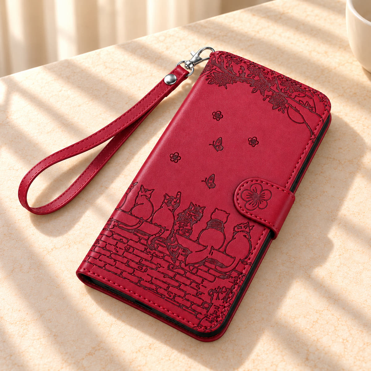 Ruby Red Cat Garden wallet case and matching wrist strap resting on a cream tabletop.