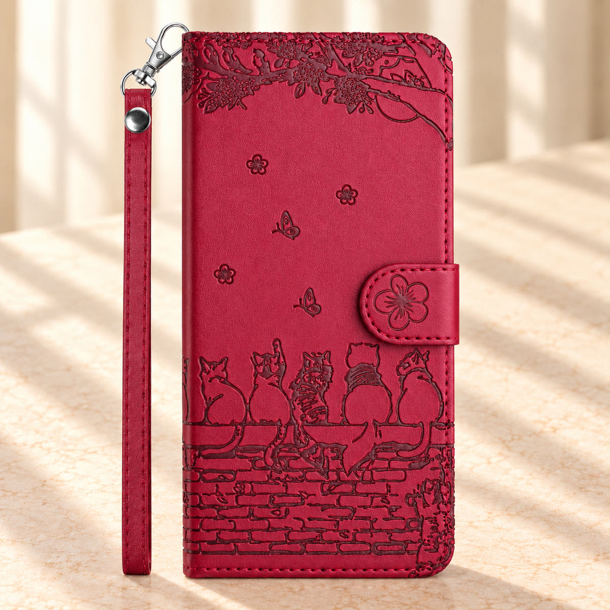 Front of the Ruby Red Cat Garden wallet case with five embossed cats, leafy branches, flower closure and wrist strap.