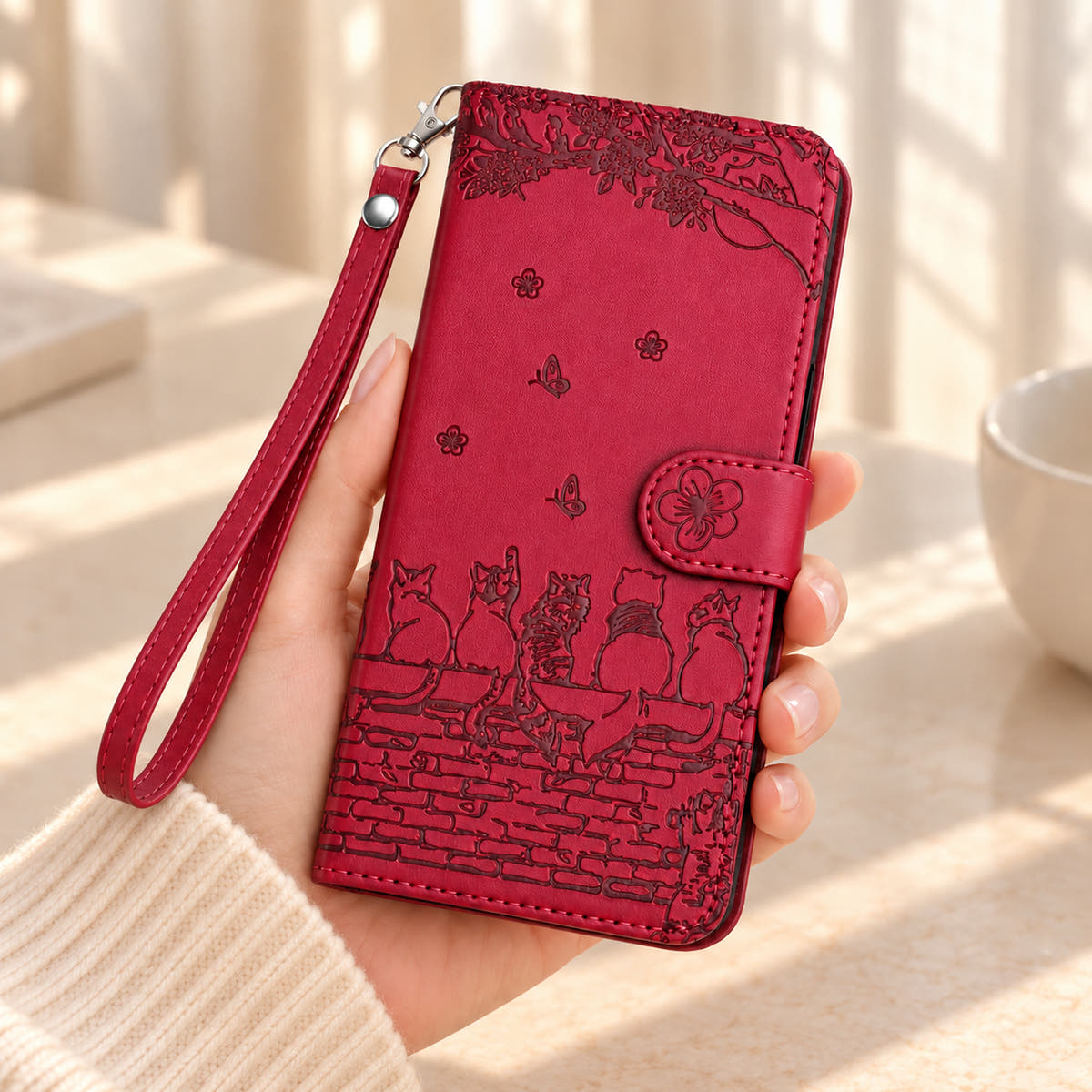 Ruby Red Cat Garden wallet case held in one hand, with its matching wrist strap and embossed garden design visible.