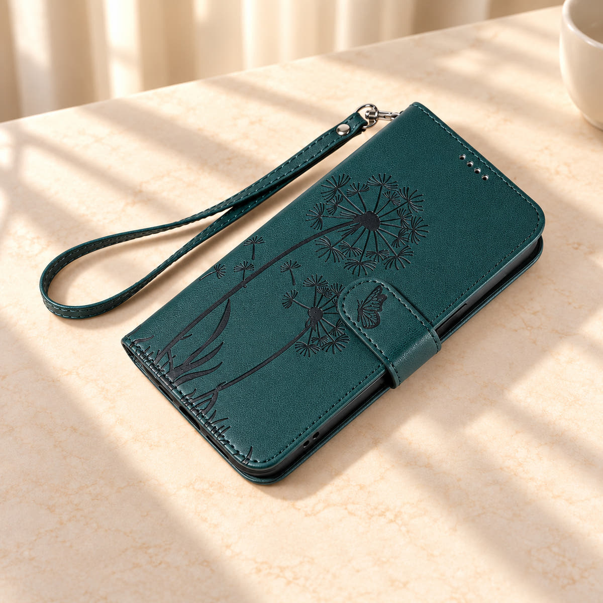 Dark Green dandelion wallet phone case lying closed with its butterfly tab and matching wrist strap.
