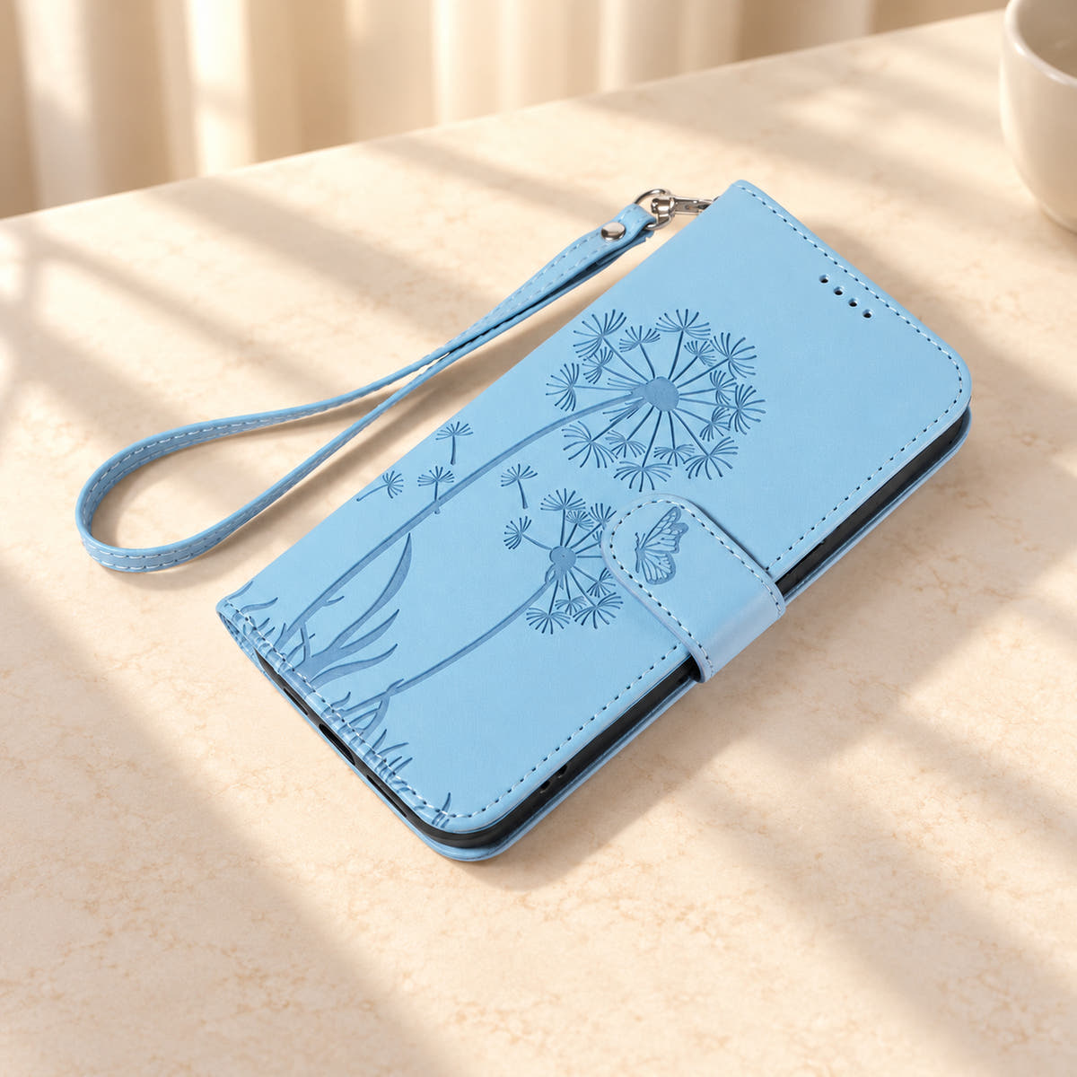 Sky Blue dandelion wallet phone case lying closed with its butterfly tab and matching wrist strap visible.