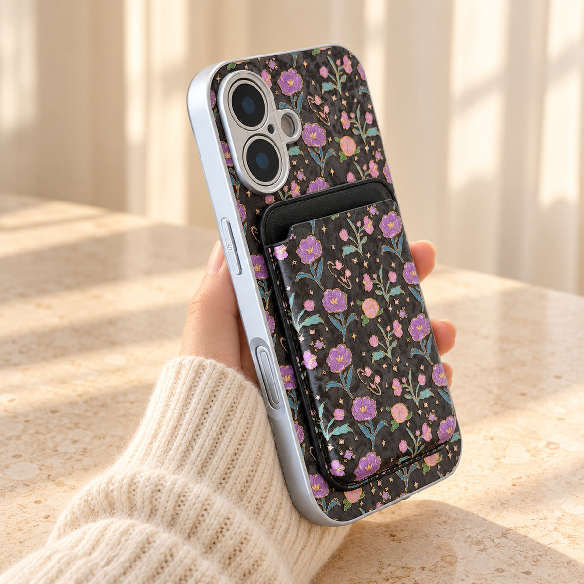 Black Elysia Floral iPhone case held in a cream-sleeved hand with its matching card wallet attached.
