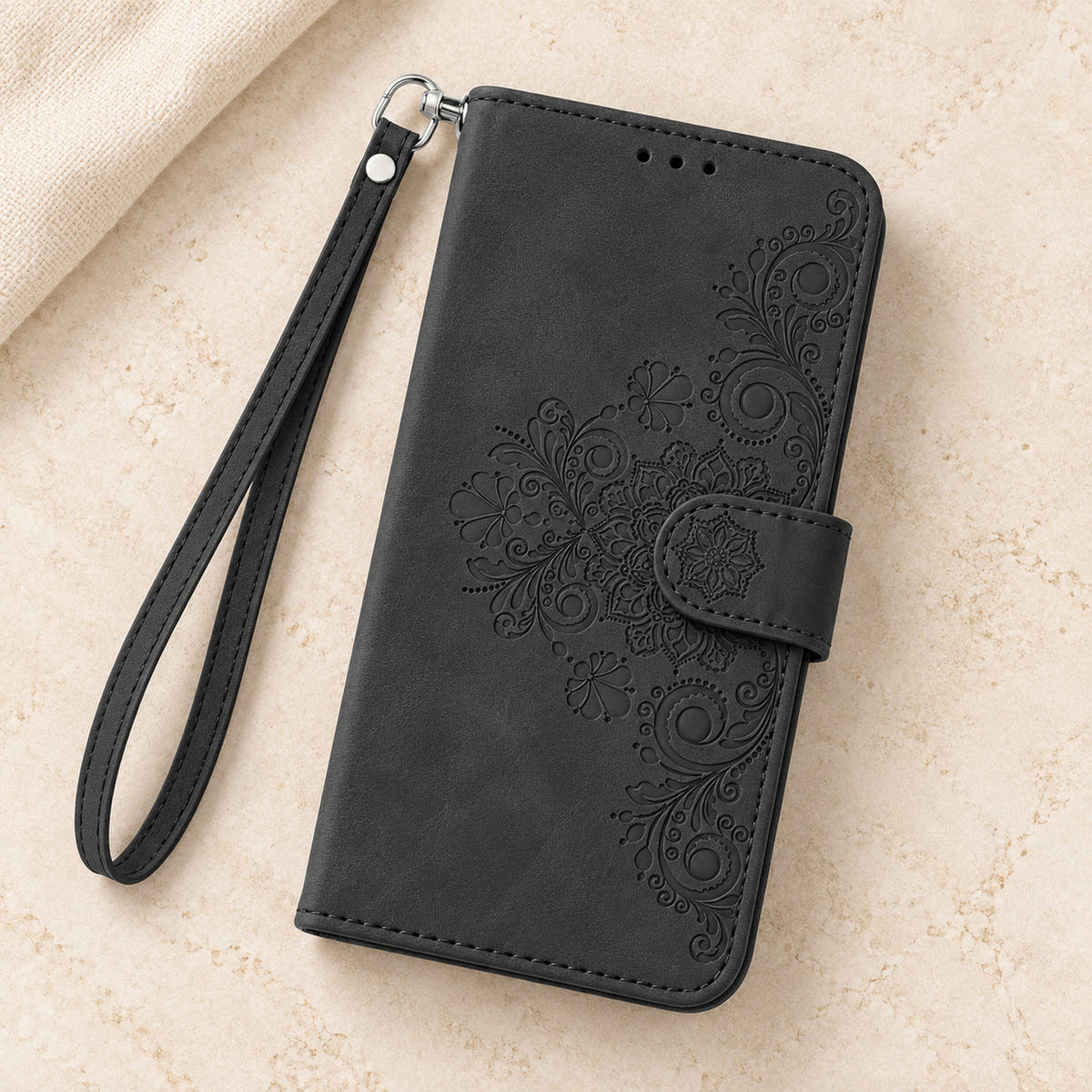 Floral embossed iPhone flip wallet case in Black — overhead view of floral front and matching wrist strap