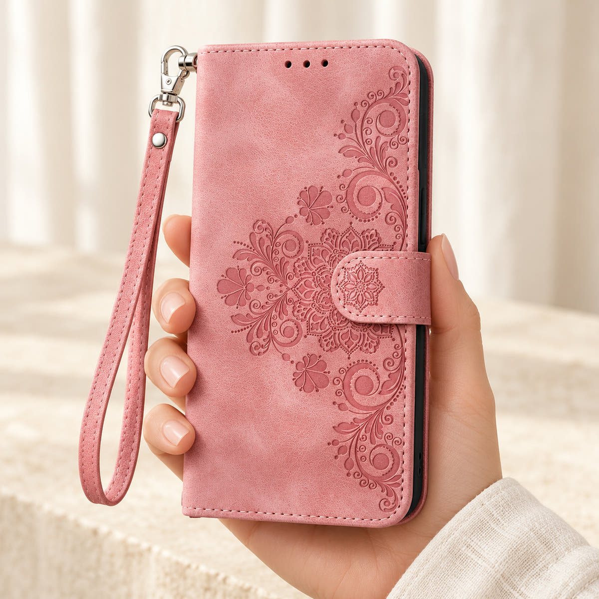 Floral embossed iPhone flip wallet case in Pink — closed front held in hand with matching wrist strap