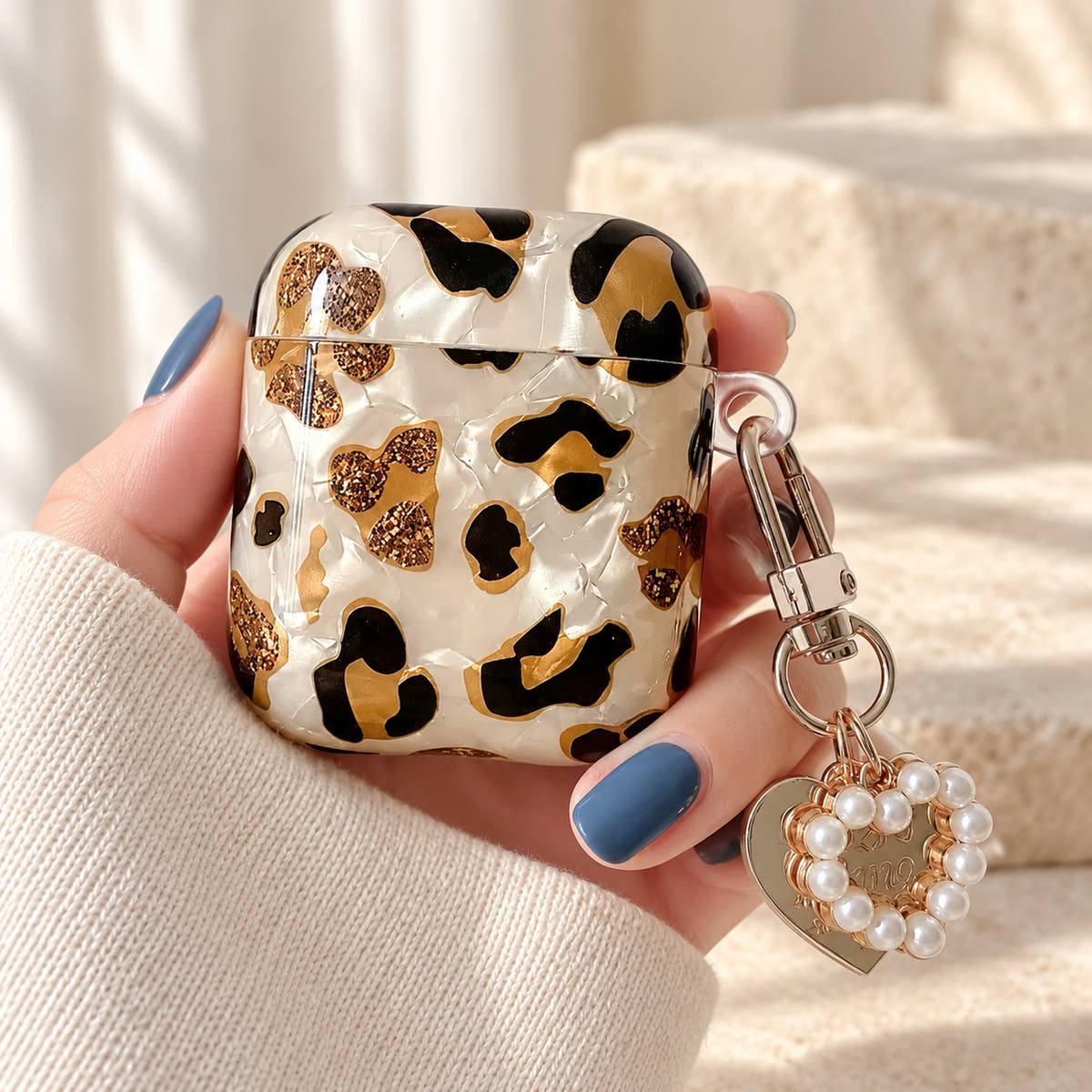 Gilded Leopard Heart AirPods case Design #2 — handheld showing its pearl-style heart charm