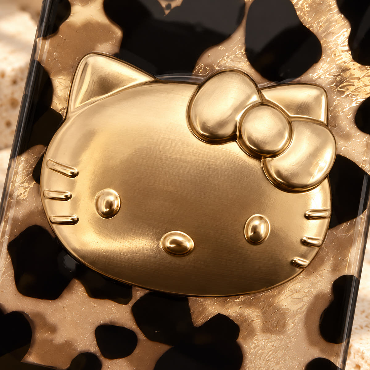 Glam Kitty case with kitty in a close-up of its raised gold-tone cat-face accent and champagne leopard surface.