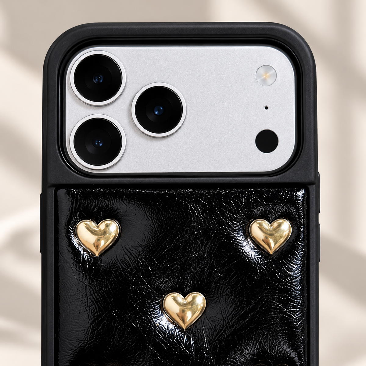 Black iPhone case with raised gold-tone hearts — camera surround and upper motif view.
