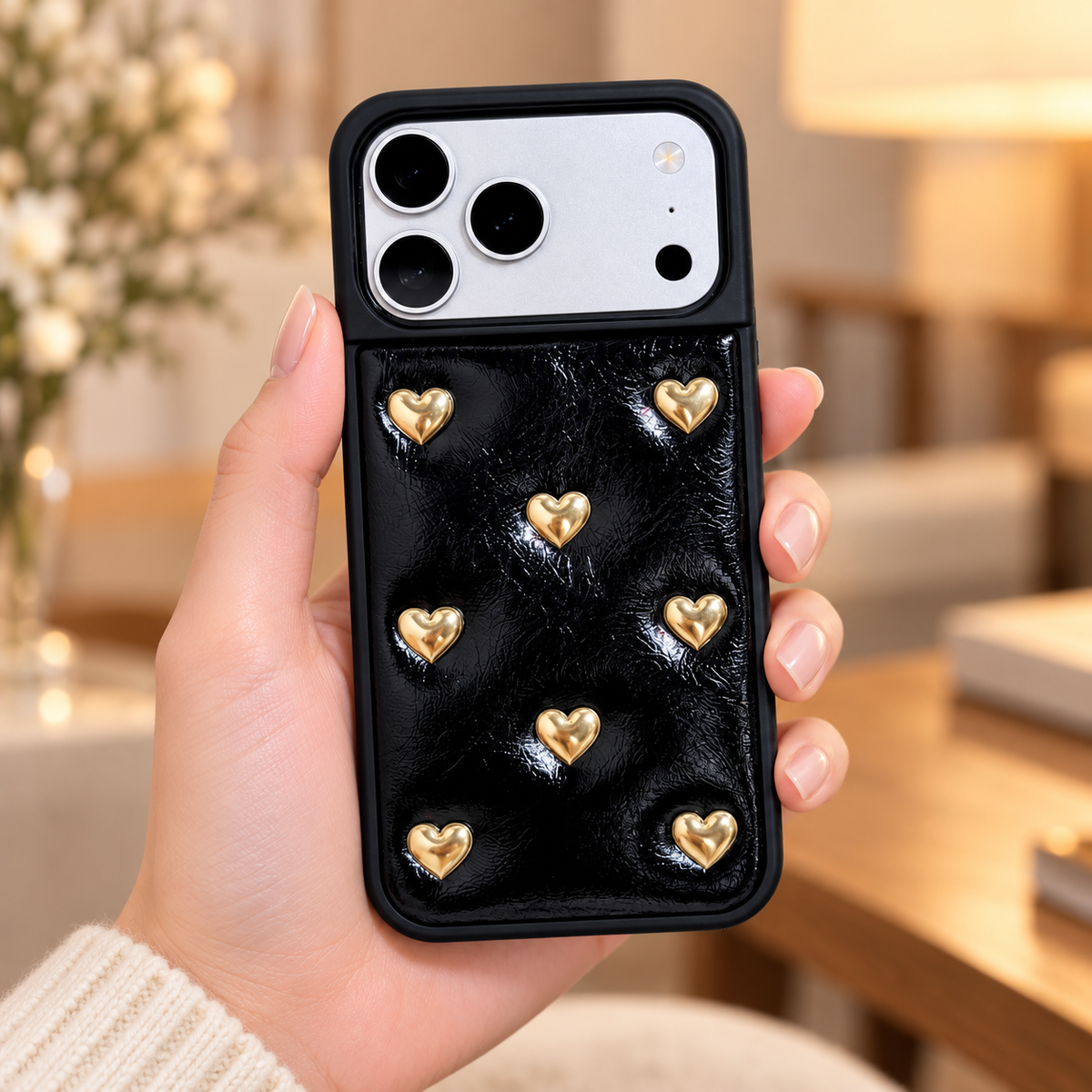 Black iPhone case with raised gold-tone hearts — handheld rear view.