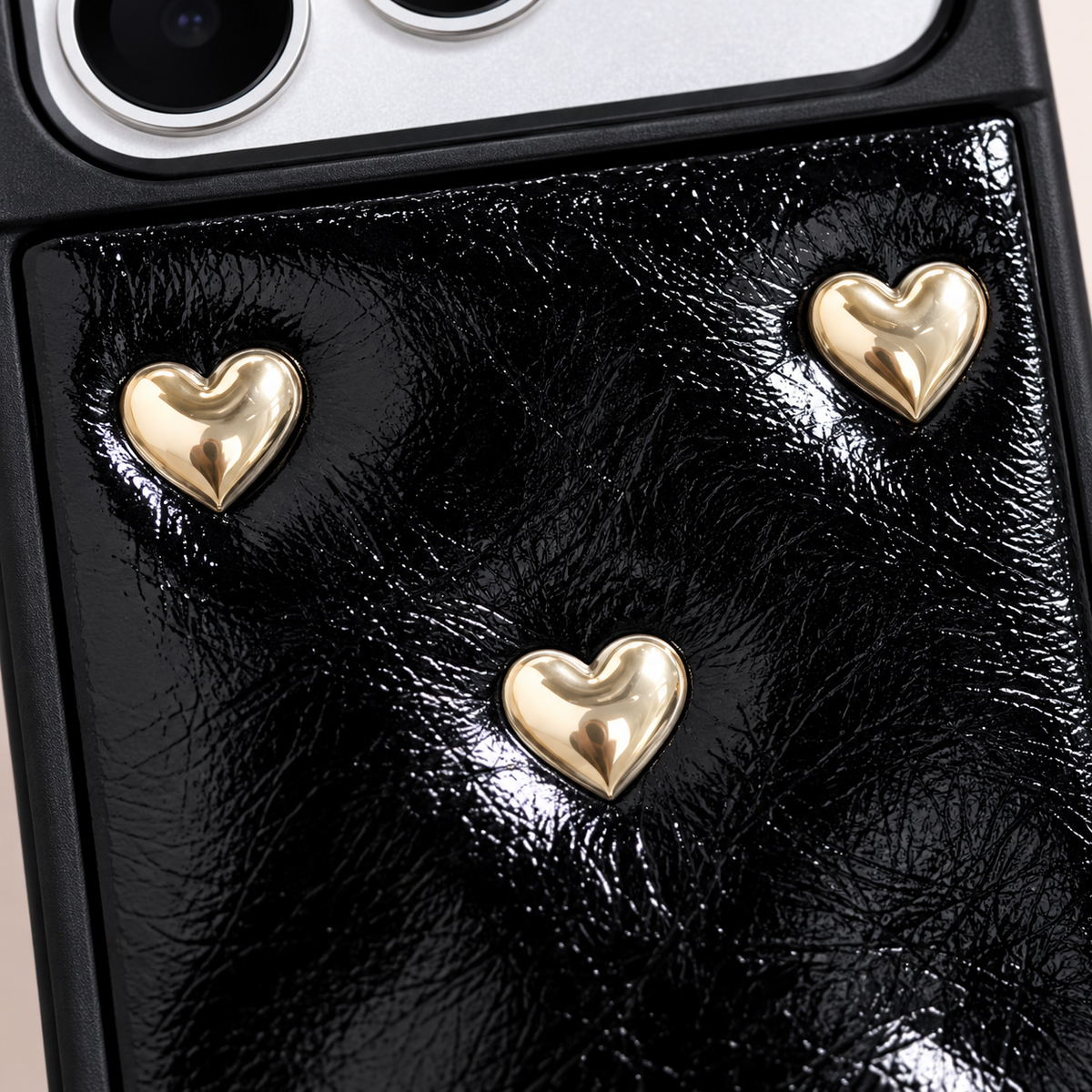 Black iPhone case with raised gold-tone hearts — gold-tone motif close-up.