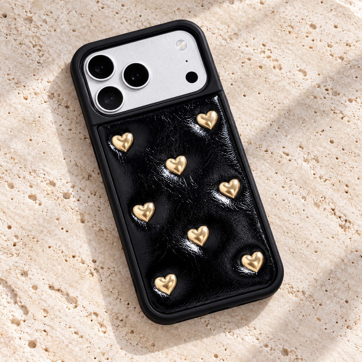 Black iPhone case with raised gold-tone hearts — angled tabletop view.