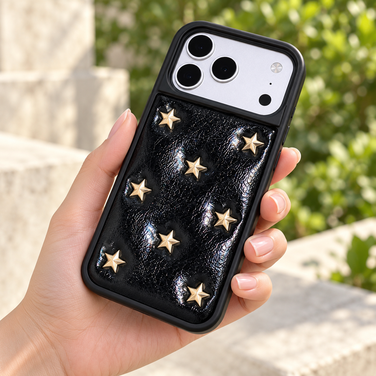 Black iPhone case with raised gold-tone stars — rear view in daylight.