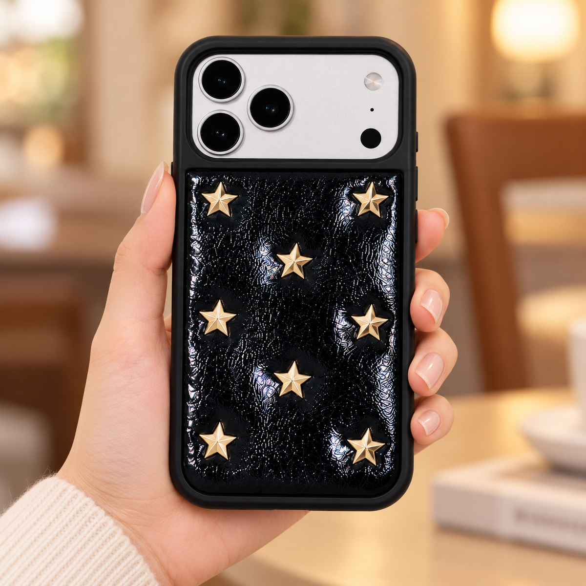 Black iPhone case with raised gold-tone stars — handheld rear view.