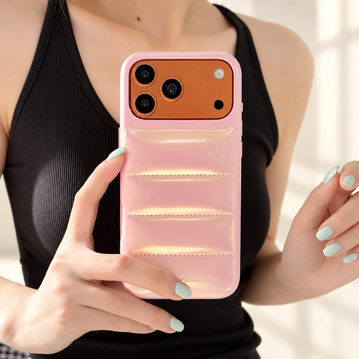 Iridescent Pink puffer case held in front of a black sleeveless outfit in warm indoor light.