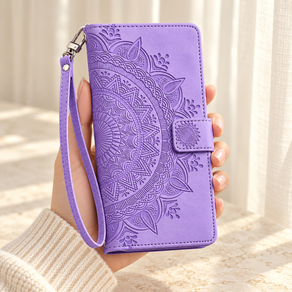 Lotus Mandala iPhone wallet case in Lavender showing the embossed front and wrist strap held in a cream-sleeve hand