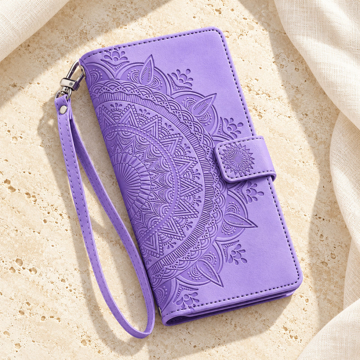 Lotus Mandala iPhone wallet case in Lavender showing the closed embossed cover and matching wrist loop on limestone
