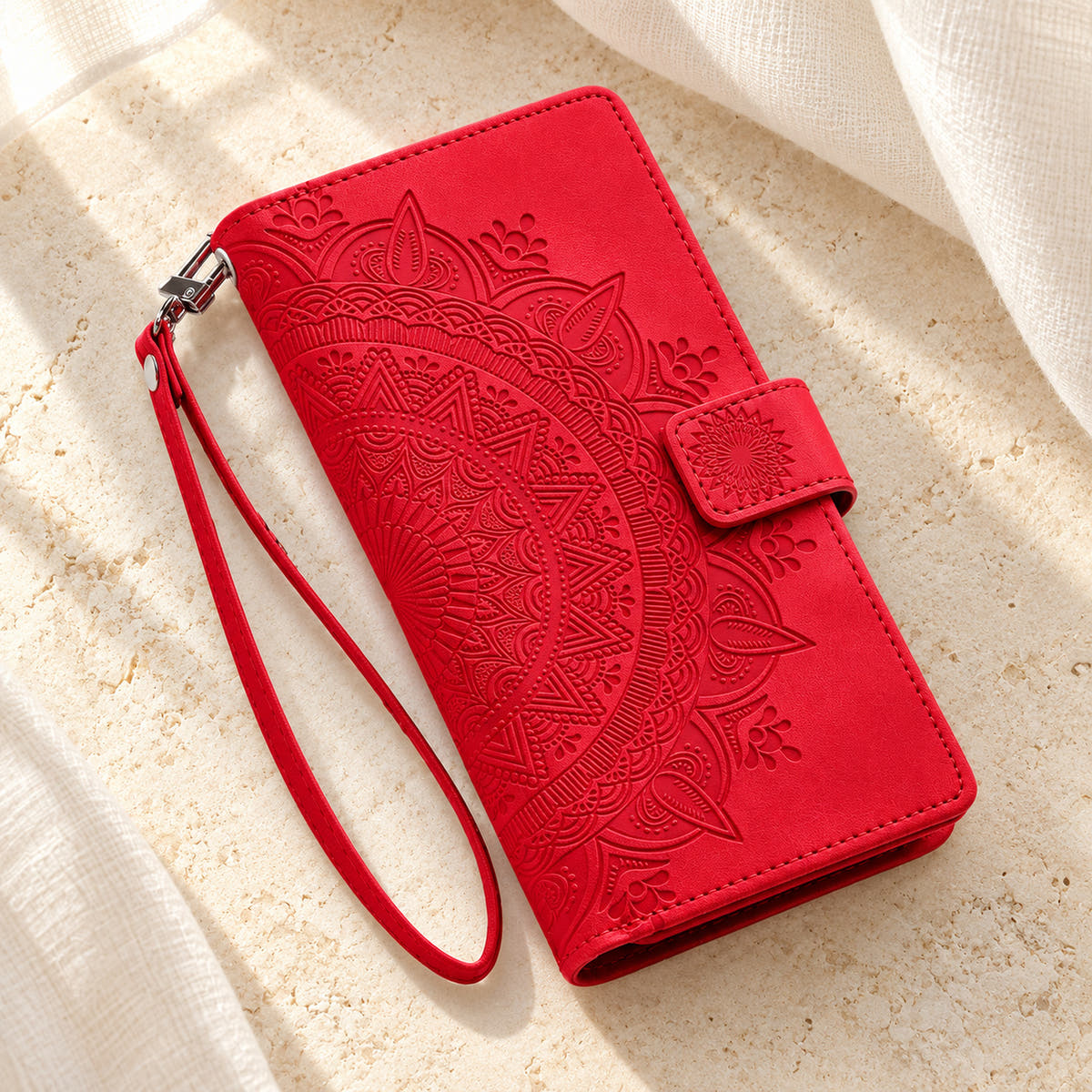 Lotus Mandala iPhone wallet case in Red showing the closed embossed cover and matching wrist loop on limestone
