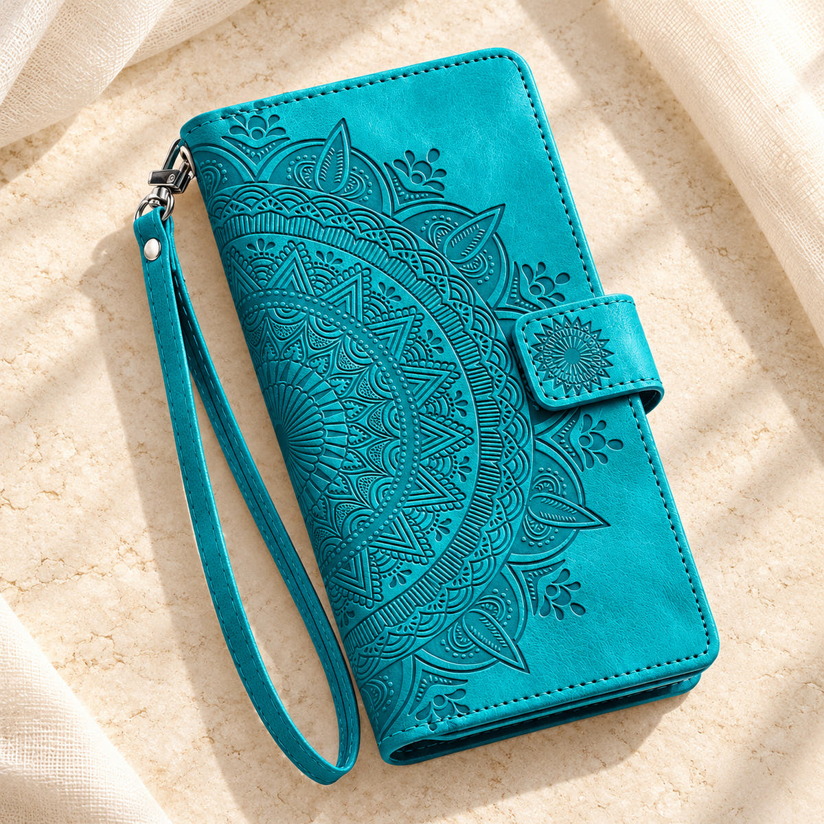 Lotus Mandala iPhone wallet case in Sea Green showing the closed embossed cover and matching wrist loop on limestone