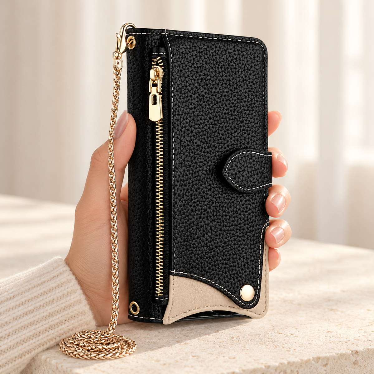 Luxe Colourblock iPhone wallet case in Black held upright, showing the zip pocket, cream contrast panel and chain