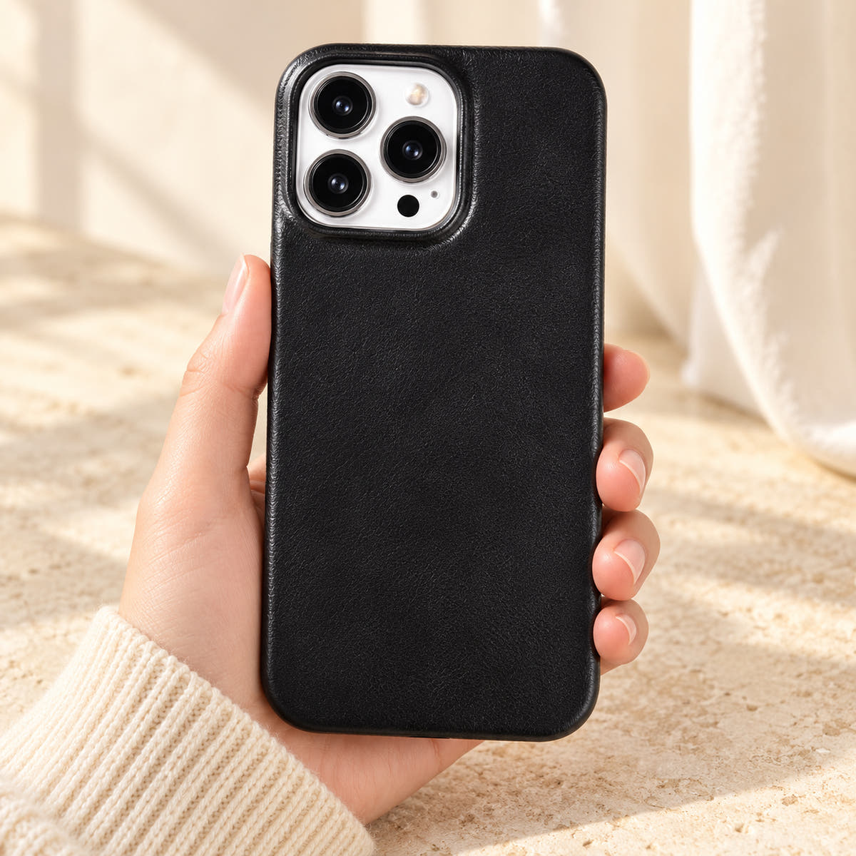 Minimal leather-look iPhone case in Black, held upright against a cream background.