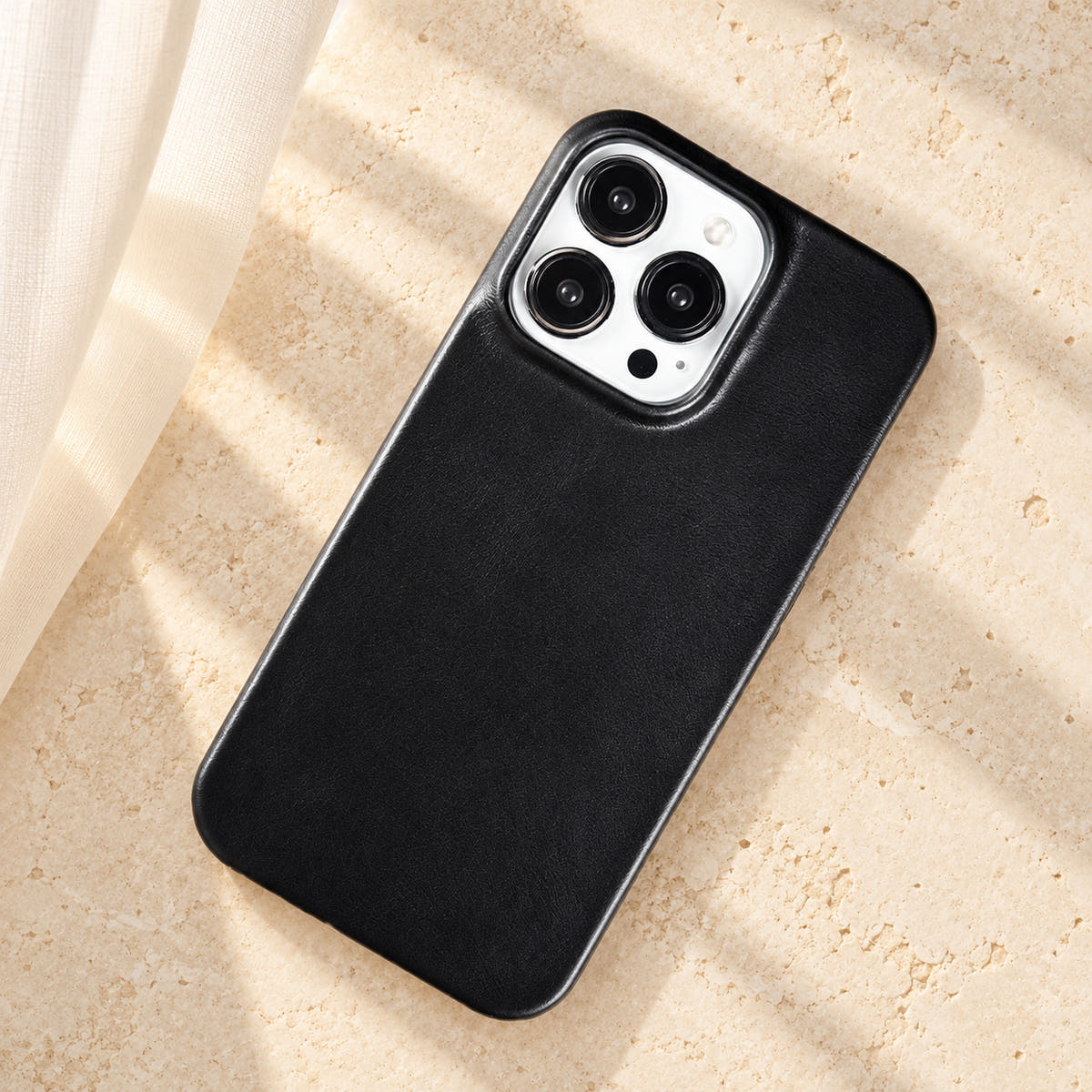 Minimal leather-look iPhone case in Black, full rear view on an ivory tabletop.