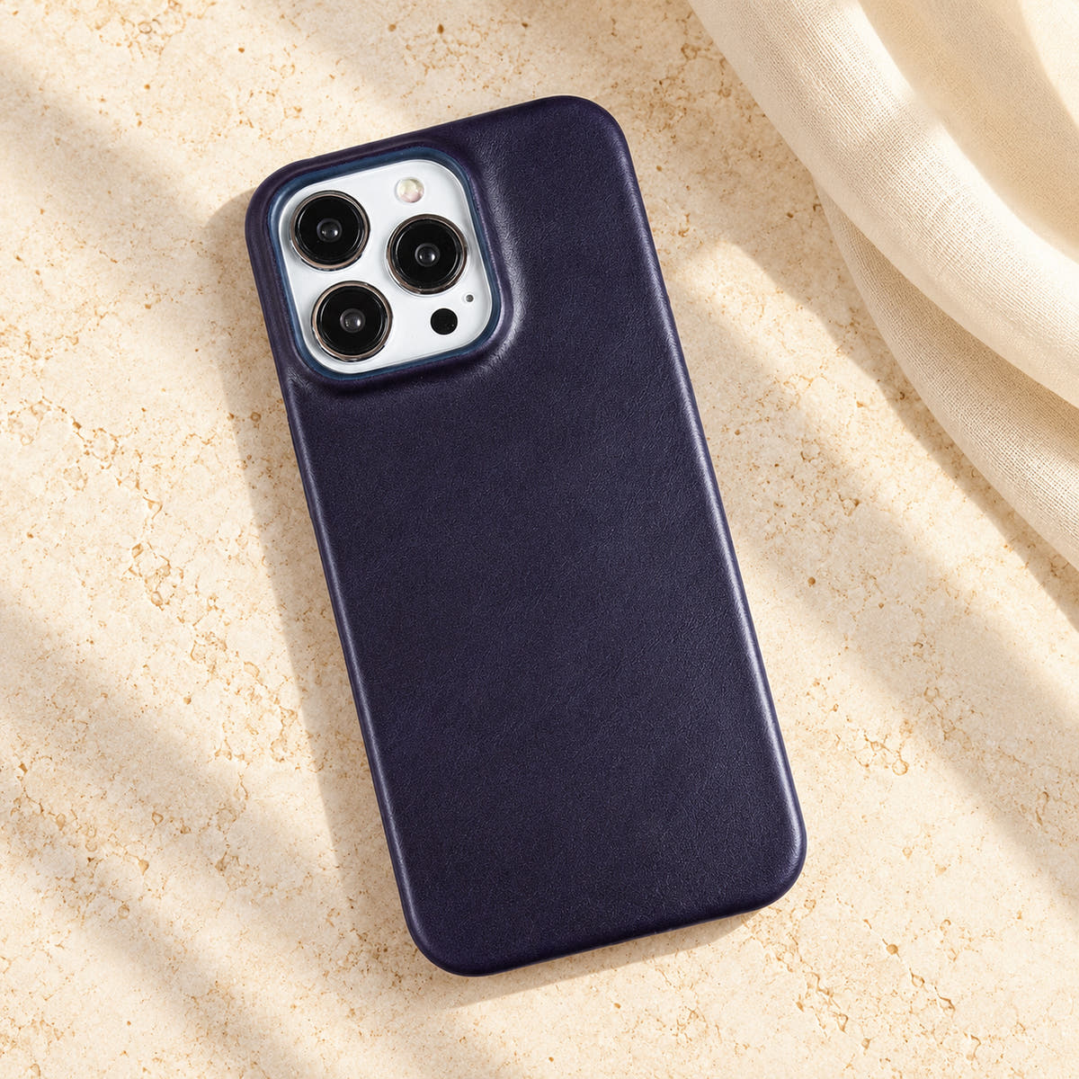 Minimal leather-look iPhone case in Dark Blue, full rear view on an ivory tabletop.