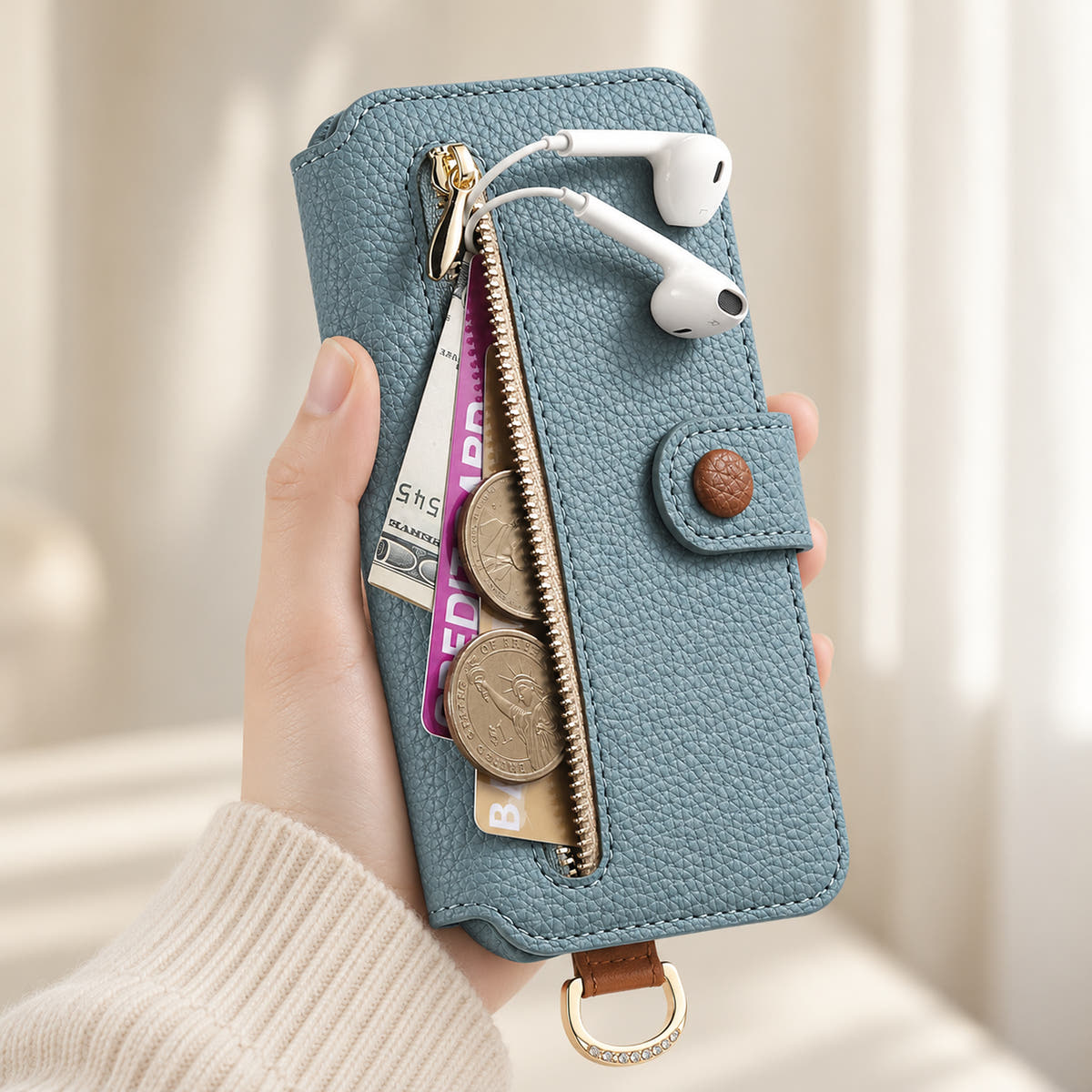 Blue iPhone wallet case with the front zip pocket open, showing illustrated cards, notes, coins and wired earphones beside the buttoned closure