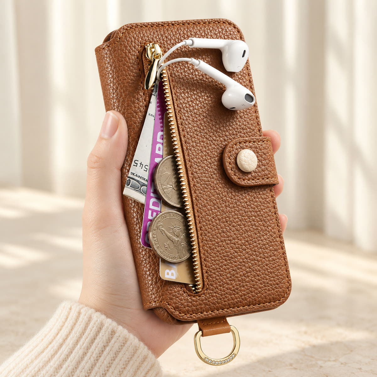 Brown iPhone wallet case with the front zip pocket open, showing illustrated cards, notes, coins and wired earphones beside the buttoned closure