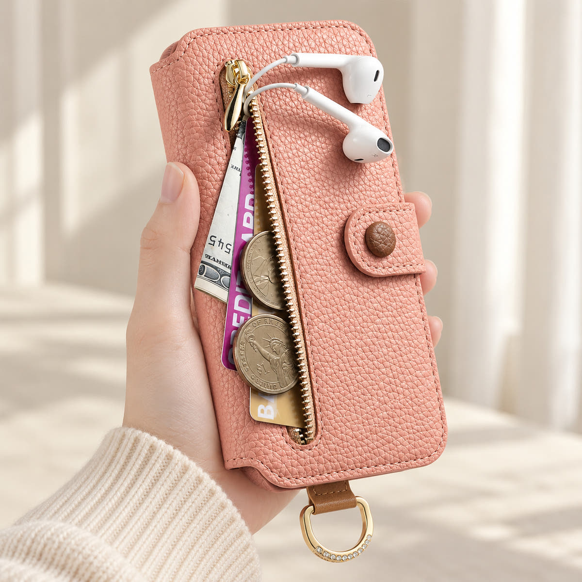 Pink iPhone wallet case with the front zip pocket open, showing illustrated cards, notes, coins and wired earphones beside the buttoned closure
