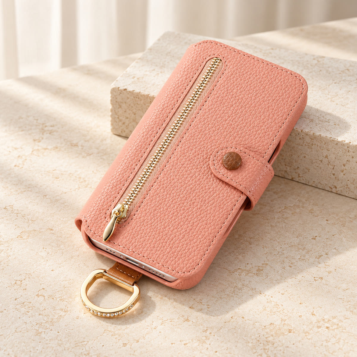 Pink textured iPhone wallet case closed on a cream surface, showing the front zip pocket, buttoned tab and attached gold-tone D-ring