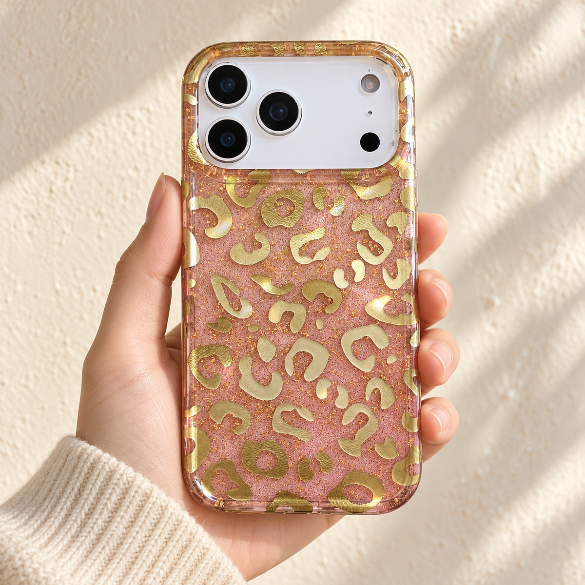 Golden Blush Leopard case held against a warm ivory wall, showing its pink sparkle and gold-tone markings.