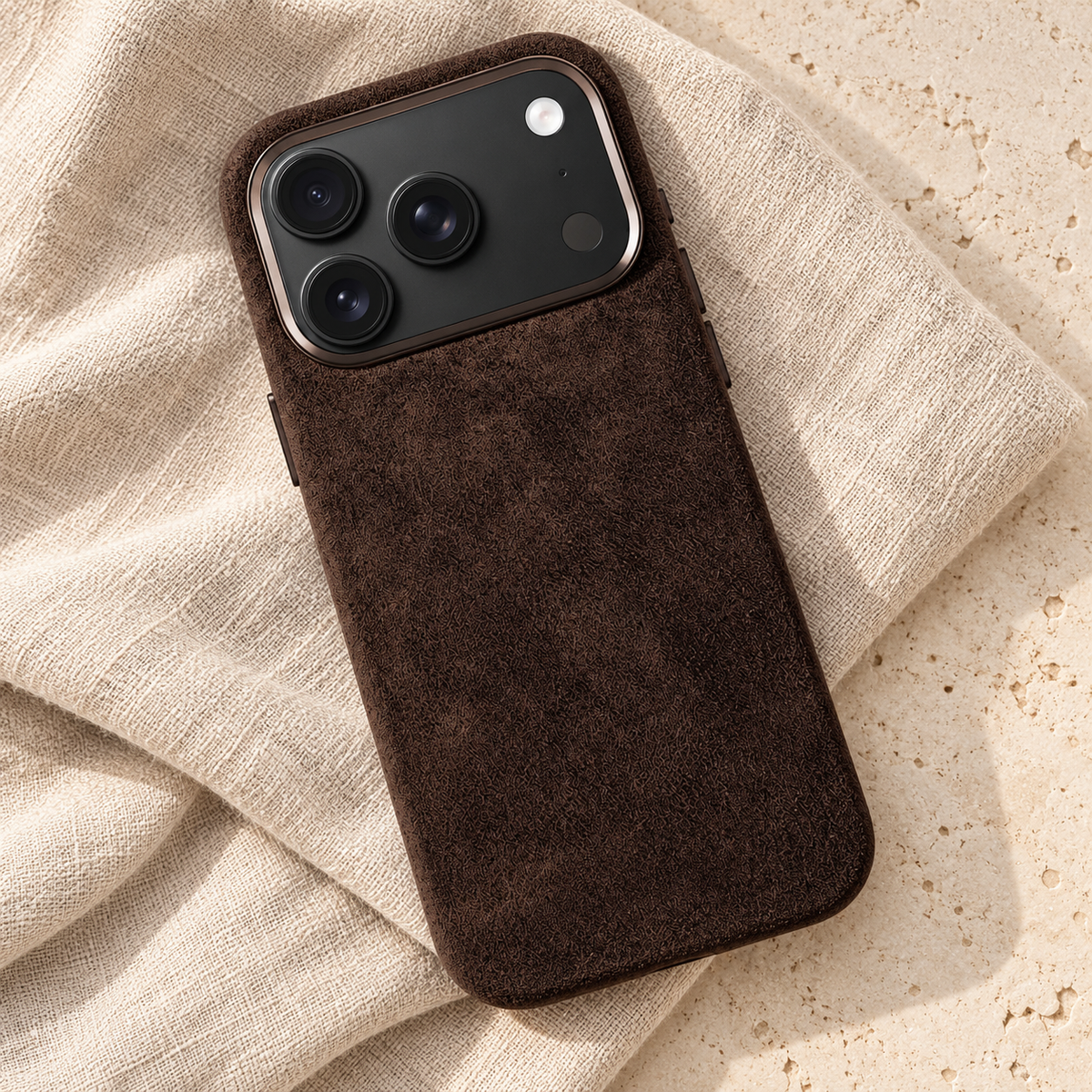 Chocolate Brown suede-look textured iPhone case in a diagonal flatlay on oatmeal linen and cream stone.