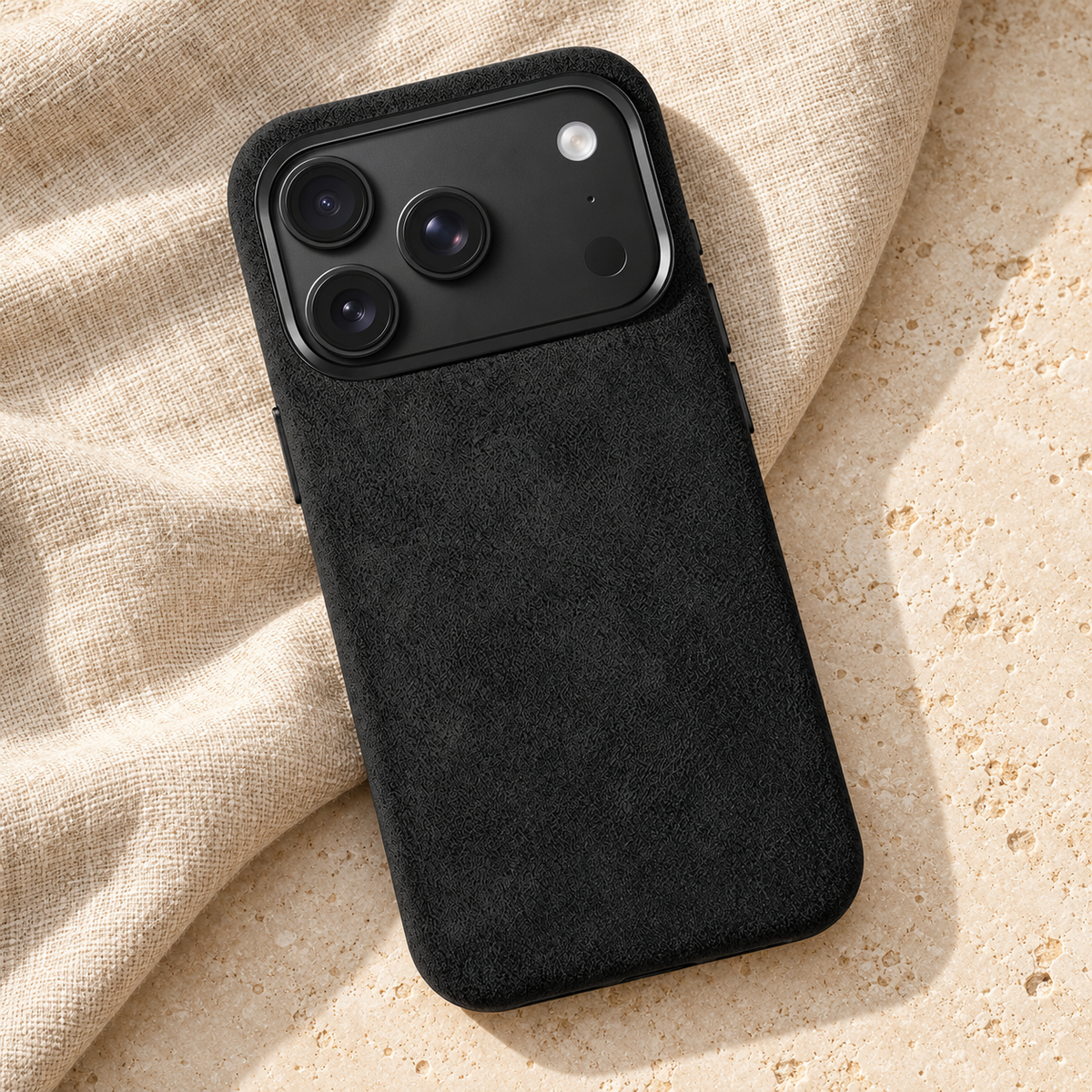 Black suede-look textured iPhone case in a diagonal flatlay on oatmeal linen and cream stone.