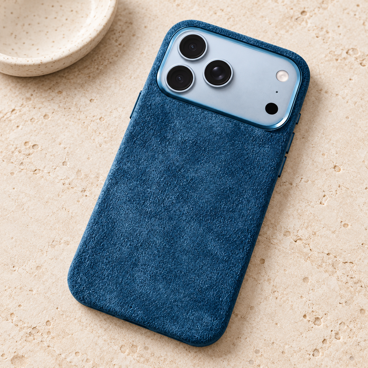 Ocean Blue suede-look textured iPhone case resting on a warm cream stone tabletop.