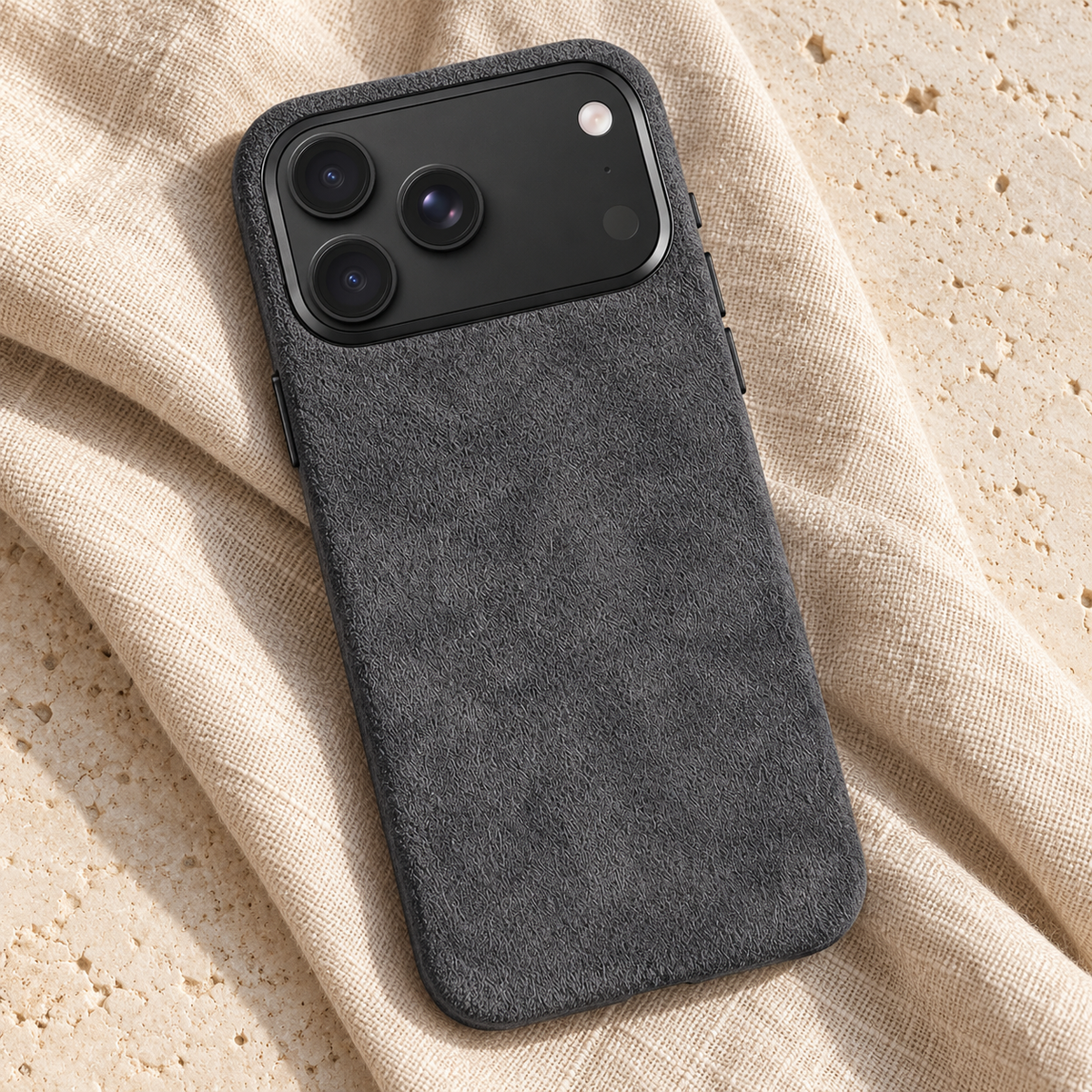 Charcoal Grey suede-look textured iPhone case in a diagonal flatlay on oatmeal linen and cream stone.