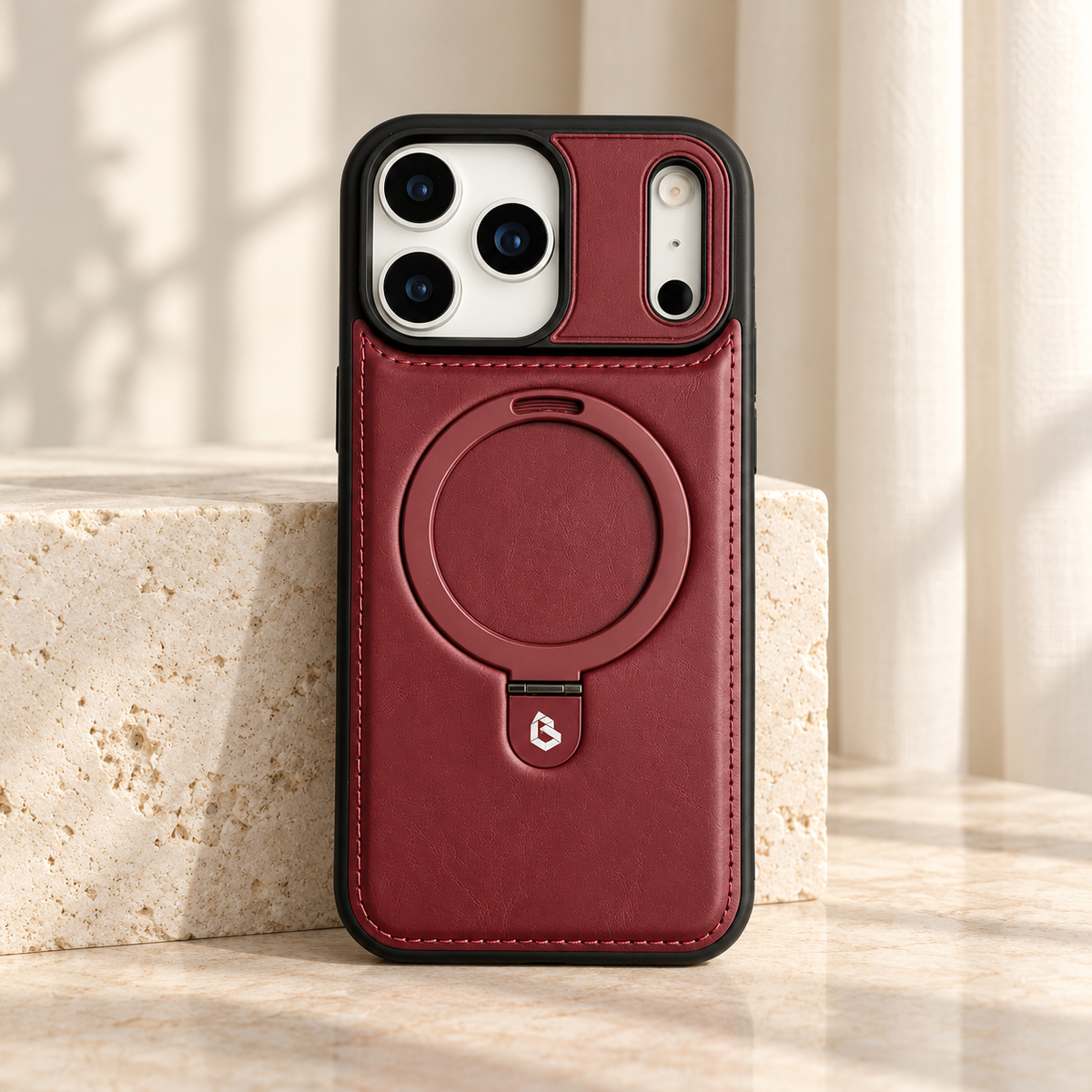 Burgundy stitched ring-stand iPhone case shown upright beside a pale stone block.