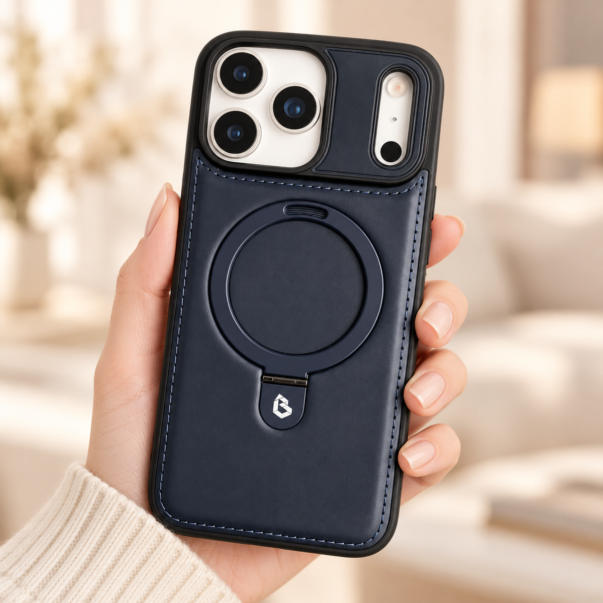Navy stitched ring-stand iPhone case held in a hand against a softly lit cream interior.