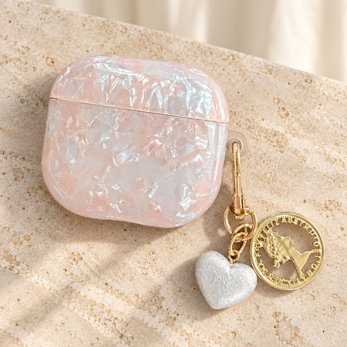 Opal Marble AirPods Case in Opal, flat lay with original attached charms on a warm cream background