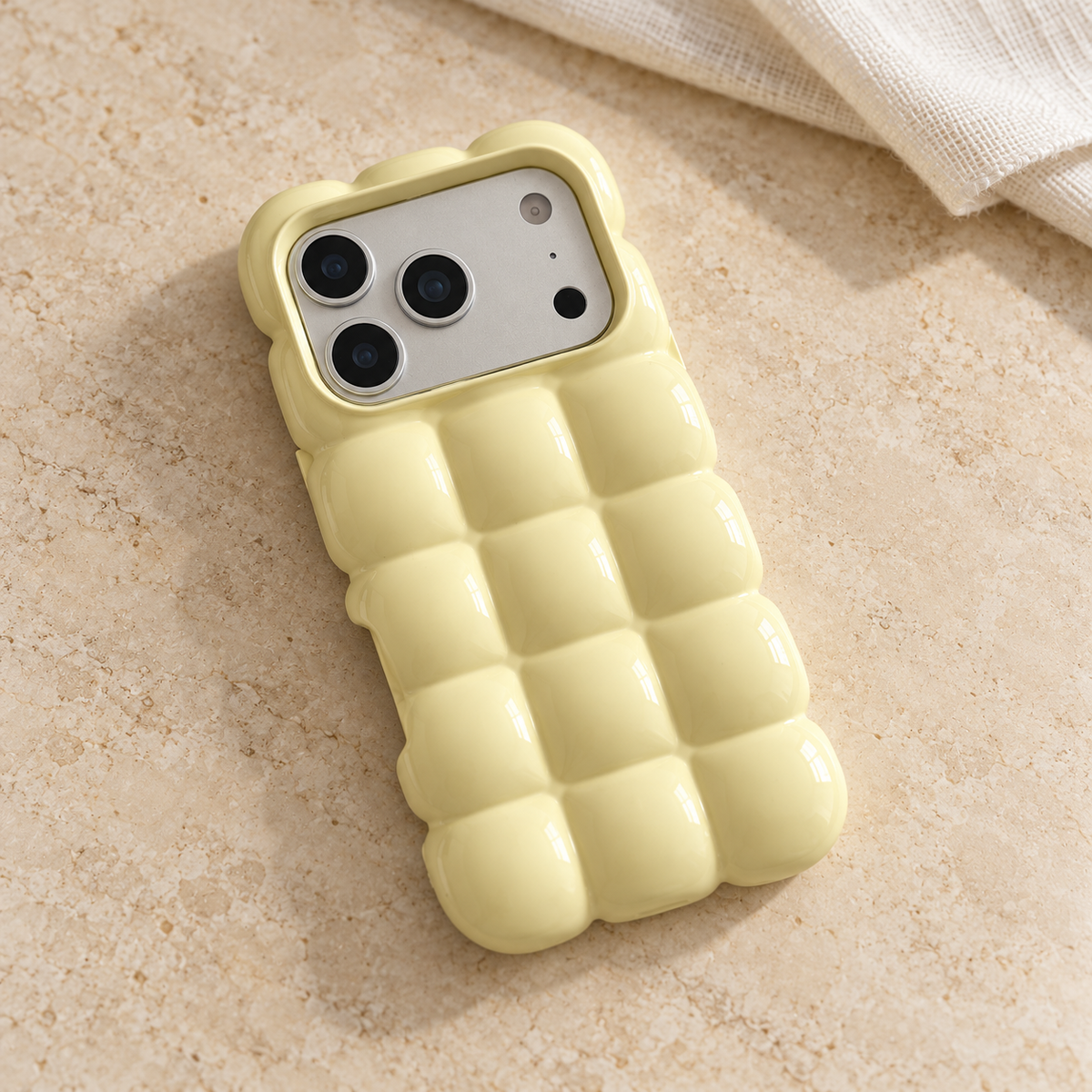 Pale Yellow puffy grid iPhone case with rounded-square back and scalloped edges — diagonal tabletop view.