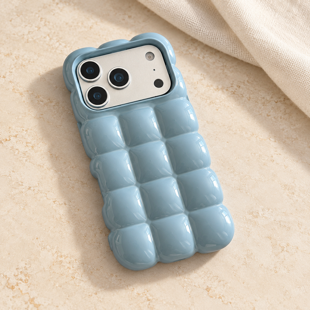 Sky Blue puffy grid iPhone case with rounded-square back and scalloped edges — diagonal tabletop view.