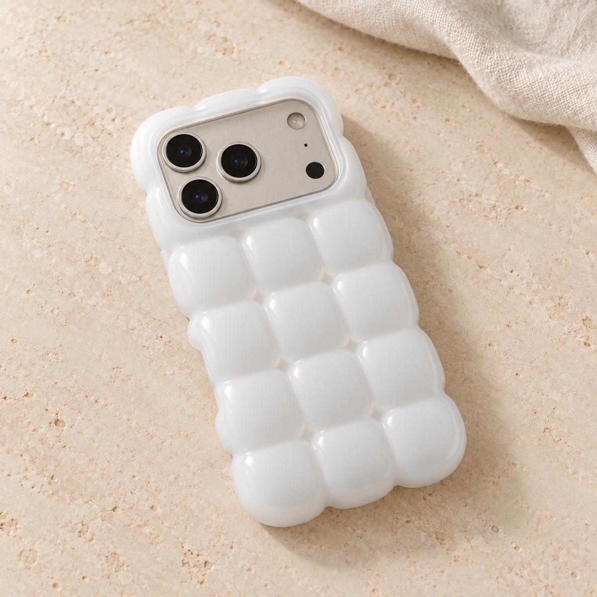 White puffy grid iPhone case with rounded-square back and scalloped edges — diagonal tabletop view.