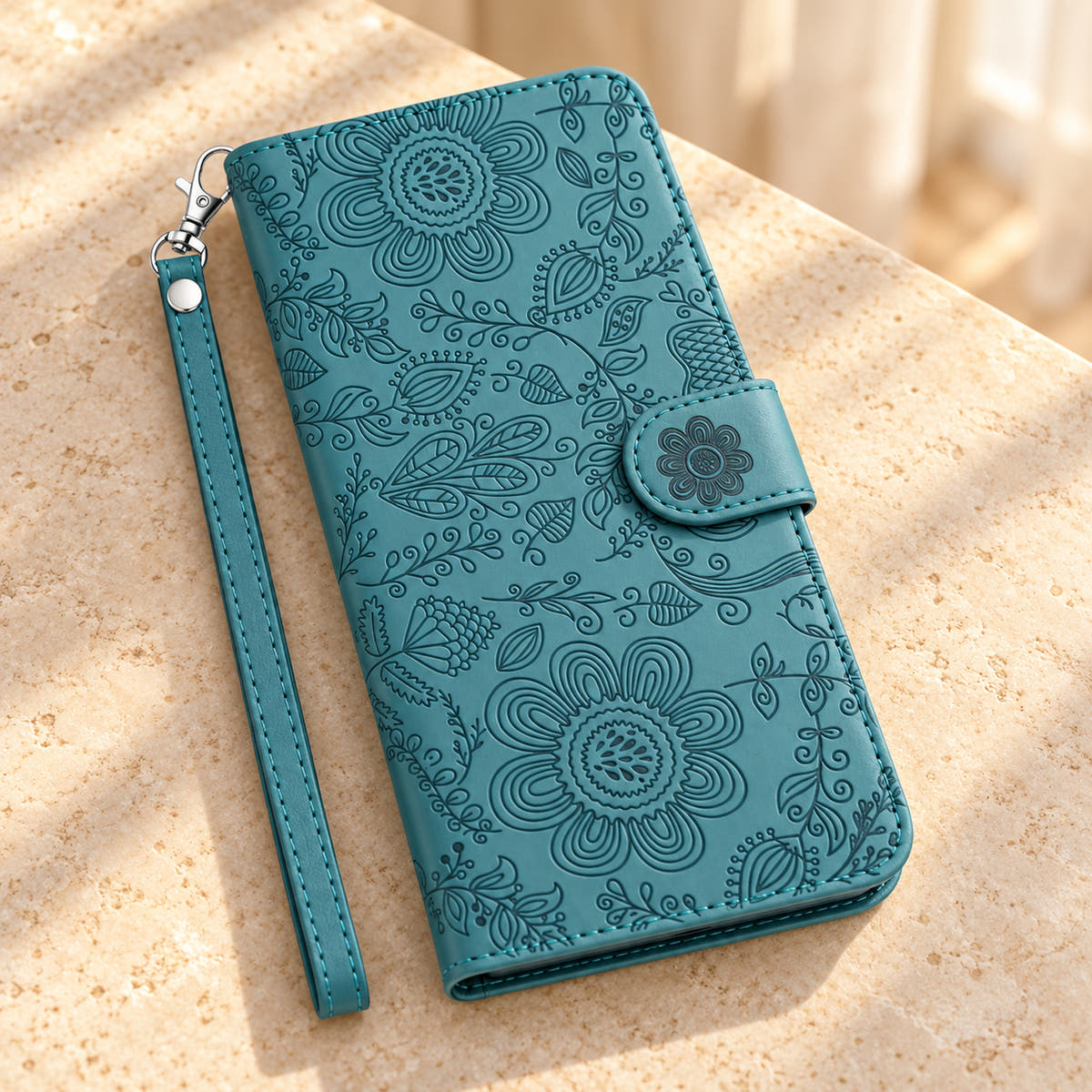 ScarletBloom Forest Green floral wallet phone case on a cream tabletop, showing the full embossed front, flower closure and single-rivet wrist loop.
