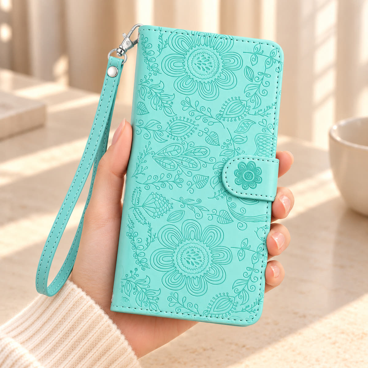 ScarletBloom Ice Blue floral wallet phone case held in a hand, showing the embossed cover, flower closure tab and matching wrist loop.