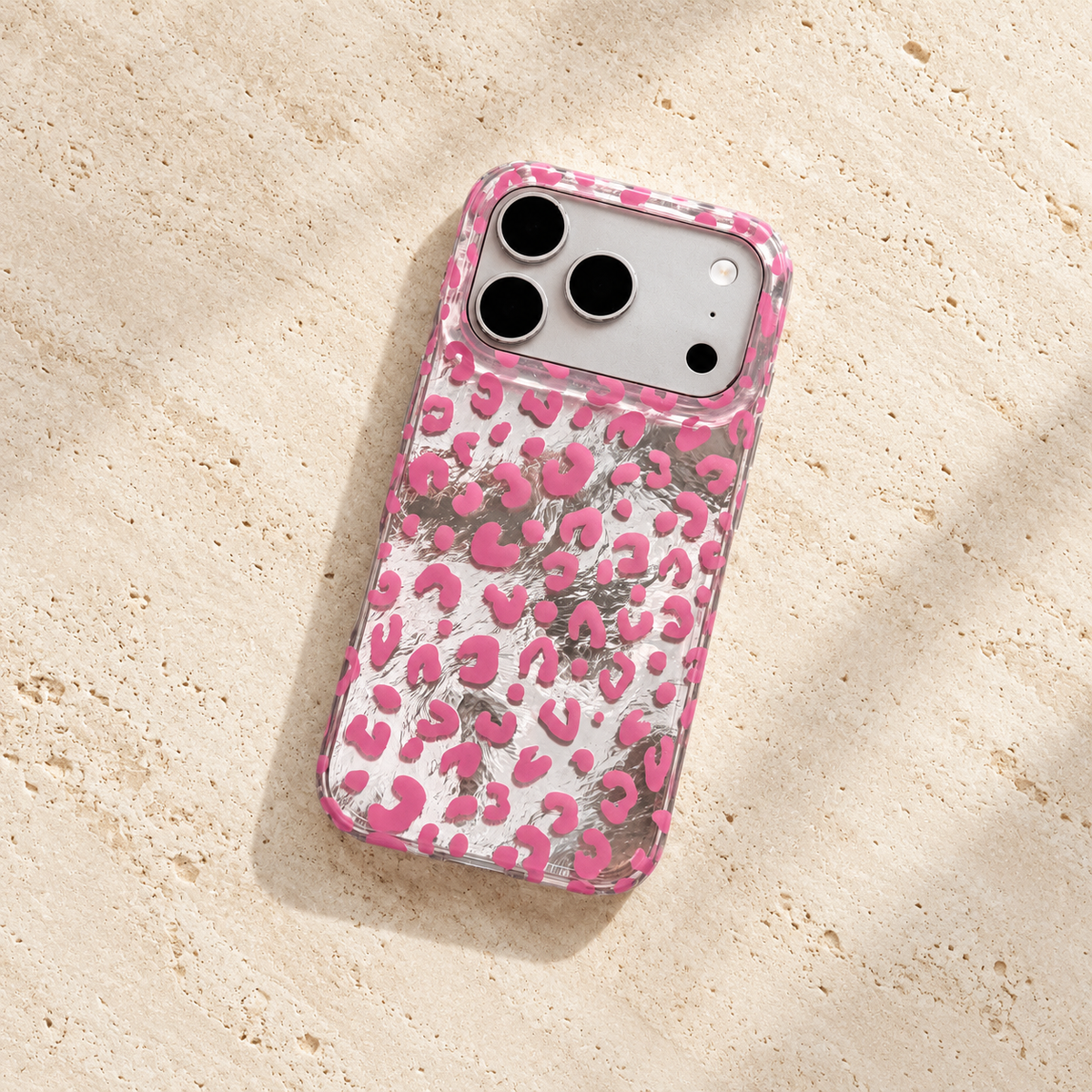 Pink leopard iPhone case lying diagonally on a cream stone tabletop with its reflective silver back visible.