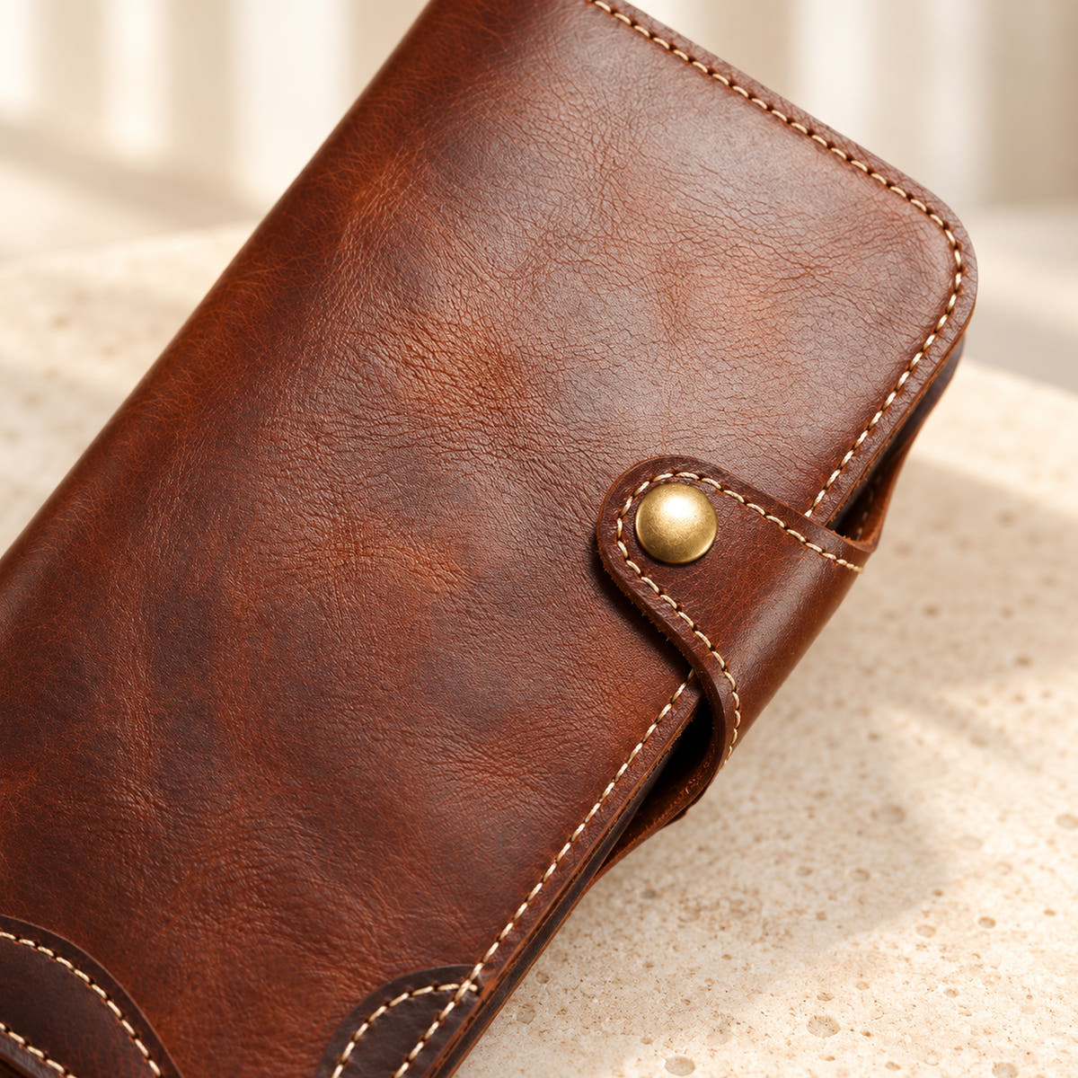 Close-up of the brown wallet case button tab, contrast stitching and textured front
