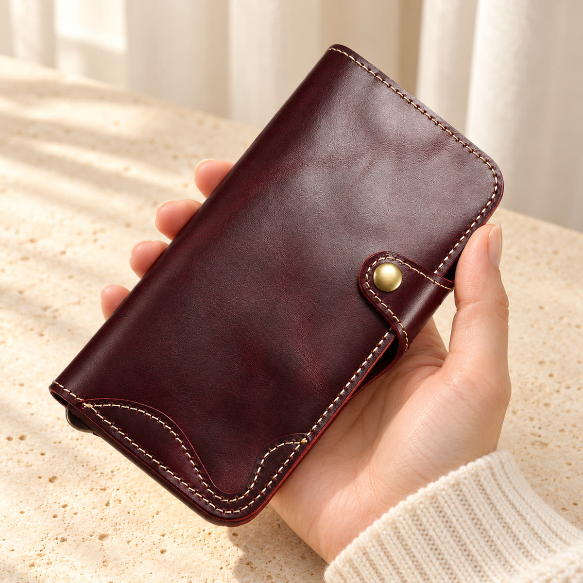 Red stitched iPhone wallet case held in one hand, showing the button tab and curved contrast stitching
