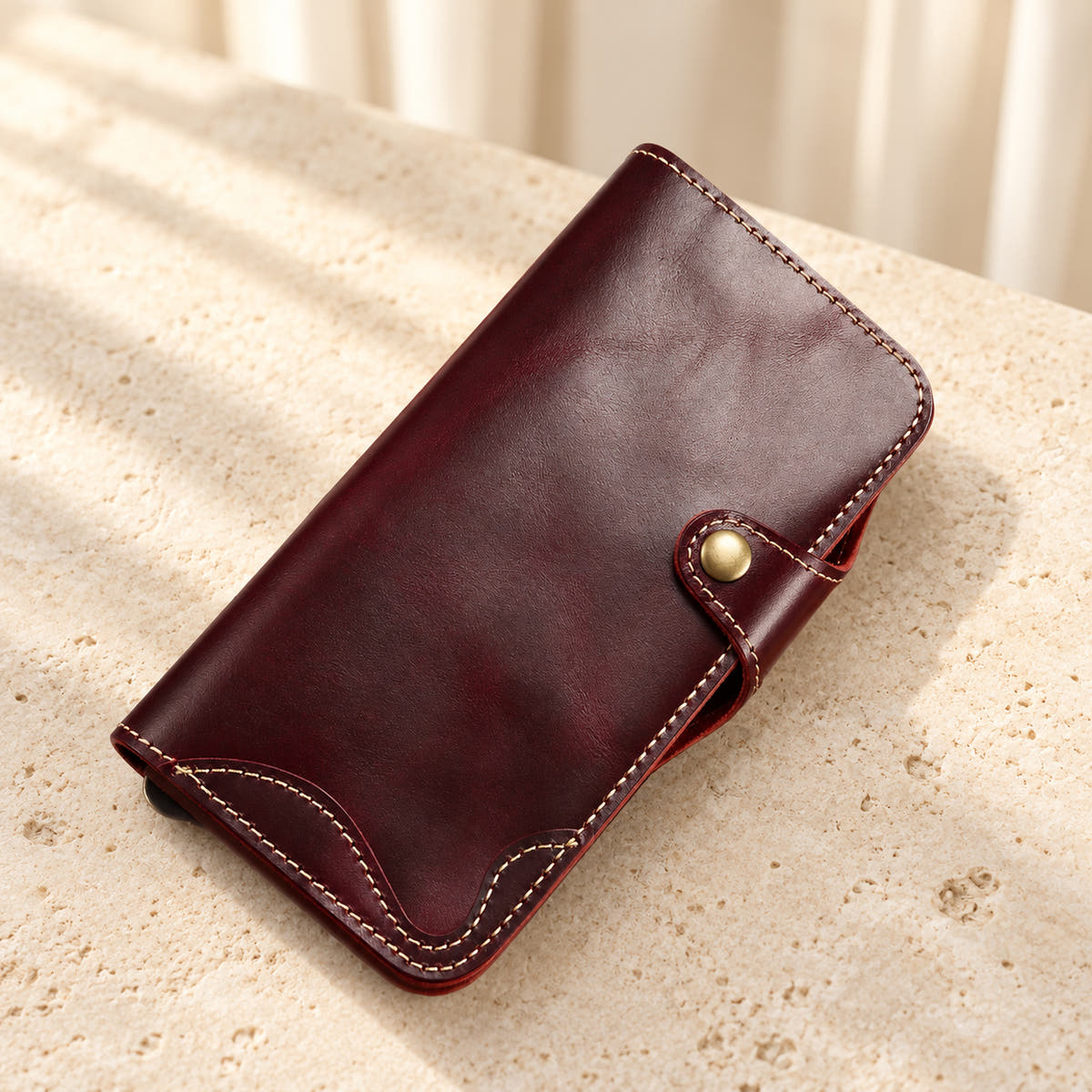 Red stitched iPhone wallet case resting on cream limestone with its front folio and button closure visible