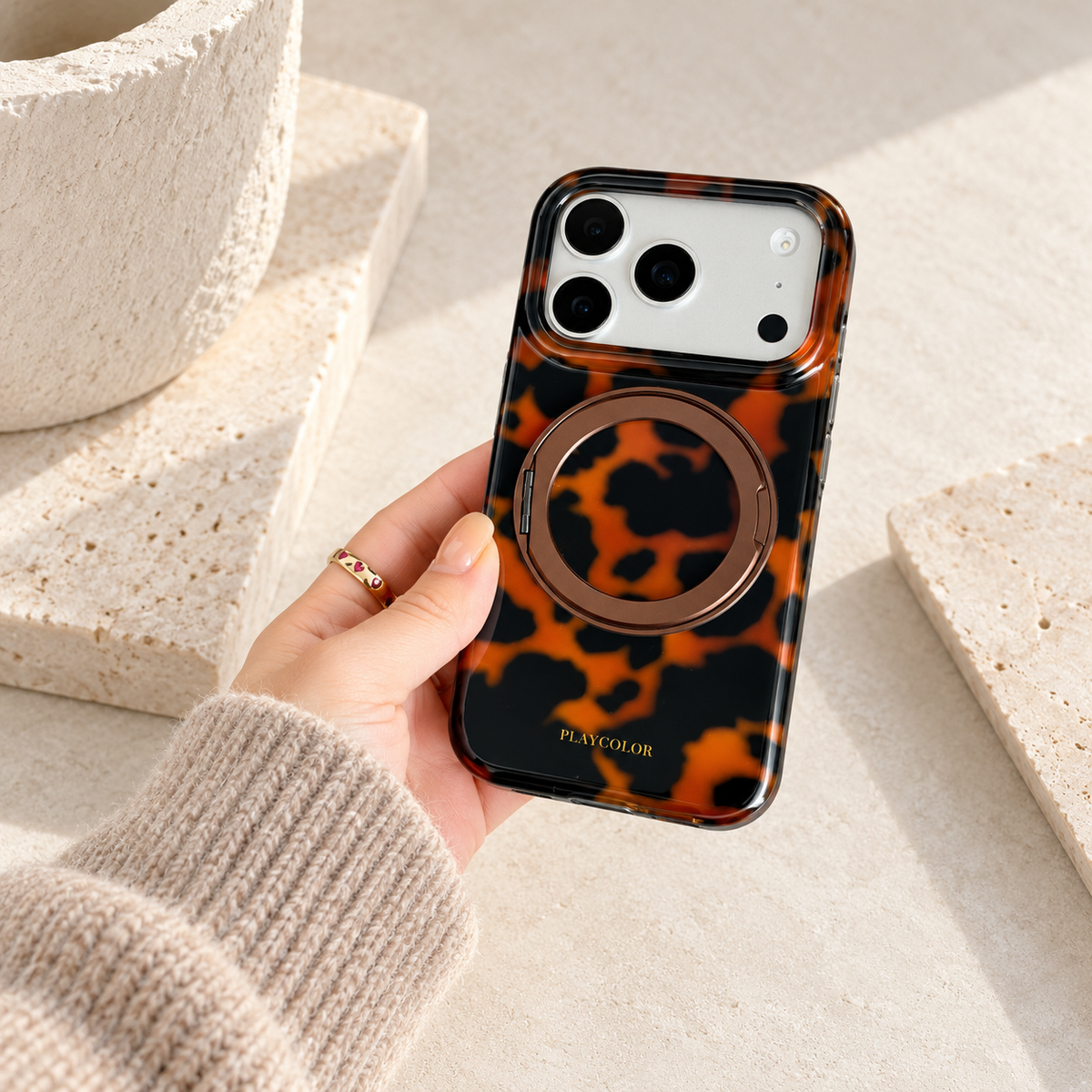 Amber tortoiseshell ring stand iPhone case held in one hand with its ring folded flat.